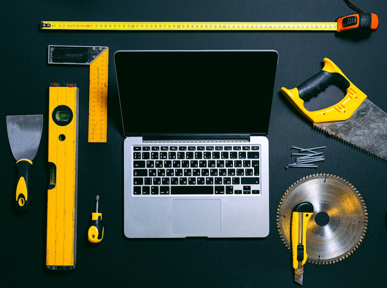 Overhead view of a laptop surrounded by various hand tools on a dark background, representing technology and construction.